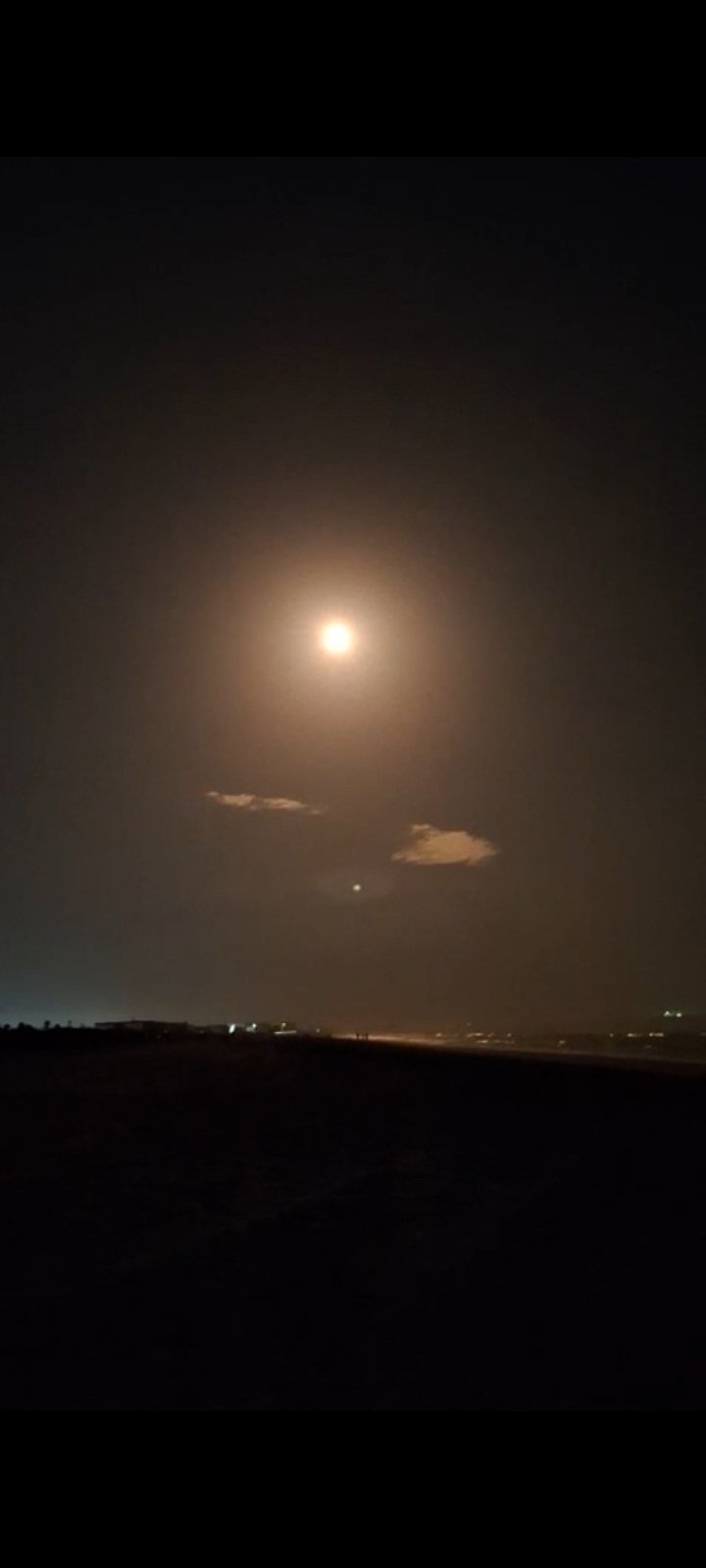 A glowing full moon over a dark South Florida coastline at night